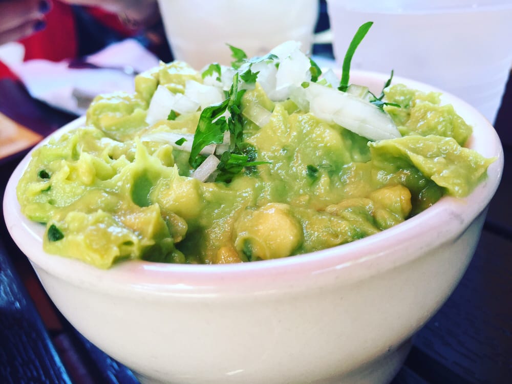 Bowl of guacamole topped with chopped onion and cilantro